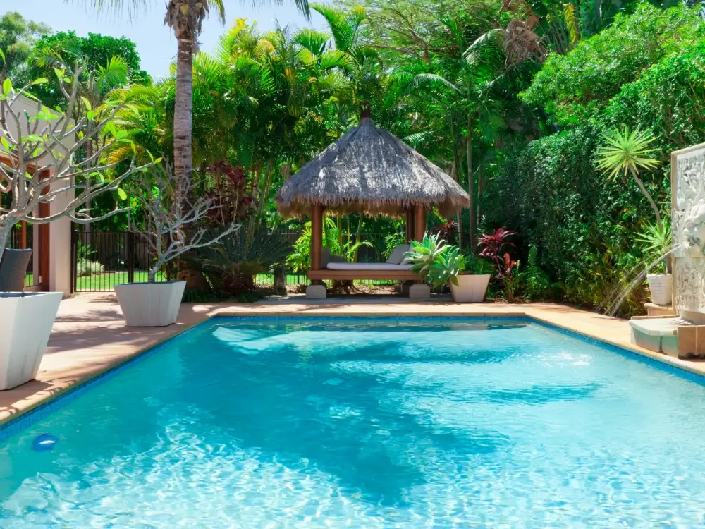 Piscine enterrée dans un jardin tropical avec paillote et végétation luxuriante