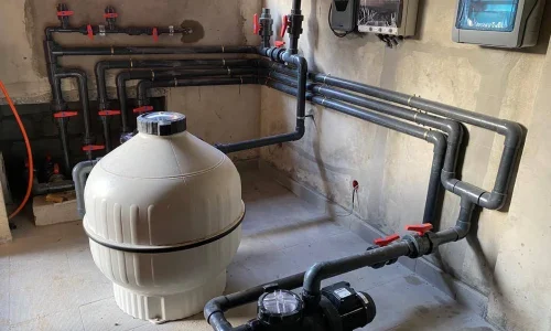 Local technique de piscine équipé d’une pompe et d’un filtre à sable reliés au circuit hydraulique